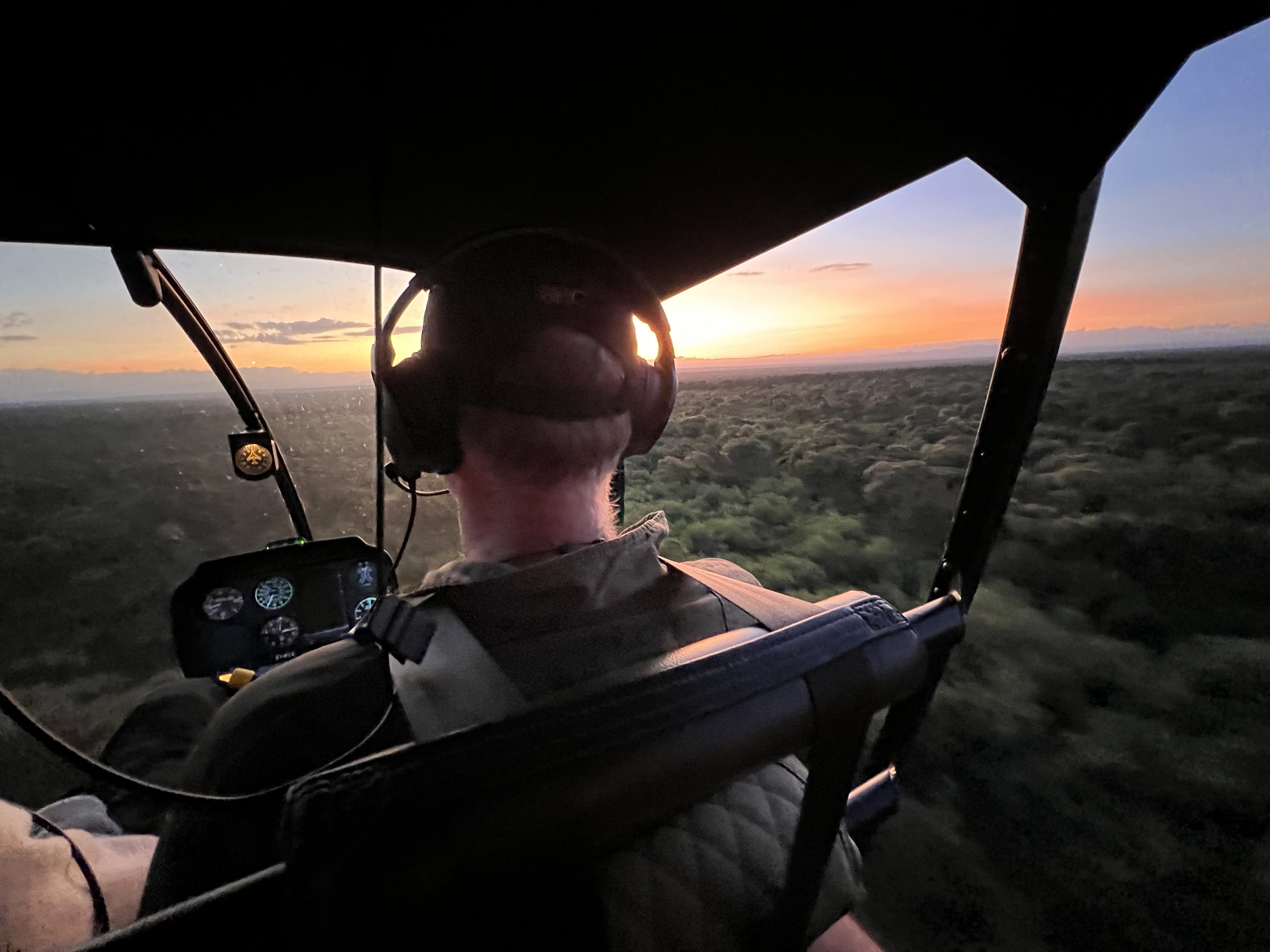 Inside a helicopter cabin at dusk, looking out over East African dryland